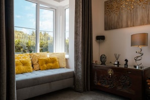 A room with a window seat, a sofa, a cabinet with decorative items, and a painting on the wall. - Perfect Booking Spacious 3-bed Home w Garden (Rochester)