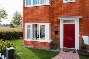 A red brick house with a white door and windows, a small garden, and a clear sky. - Perfect Booking Spacious 3-bed Home w Garden (Rochester)