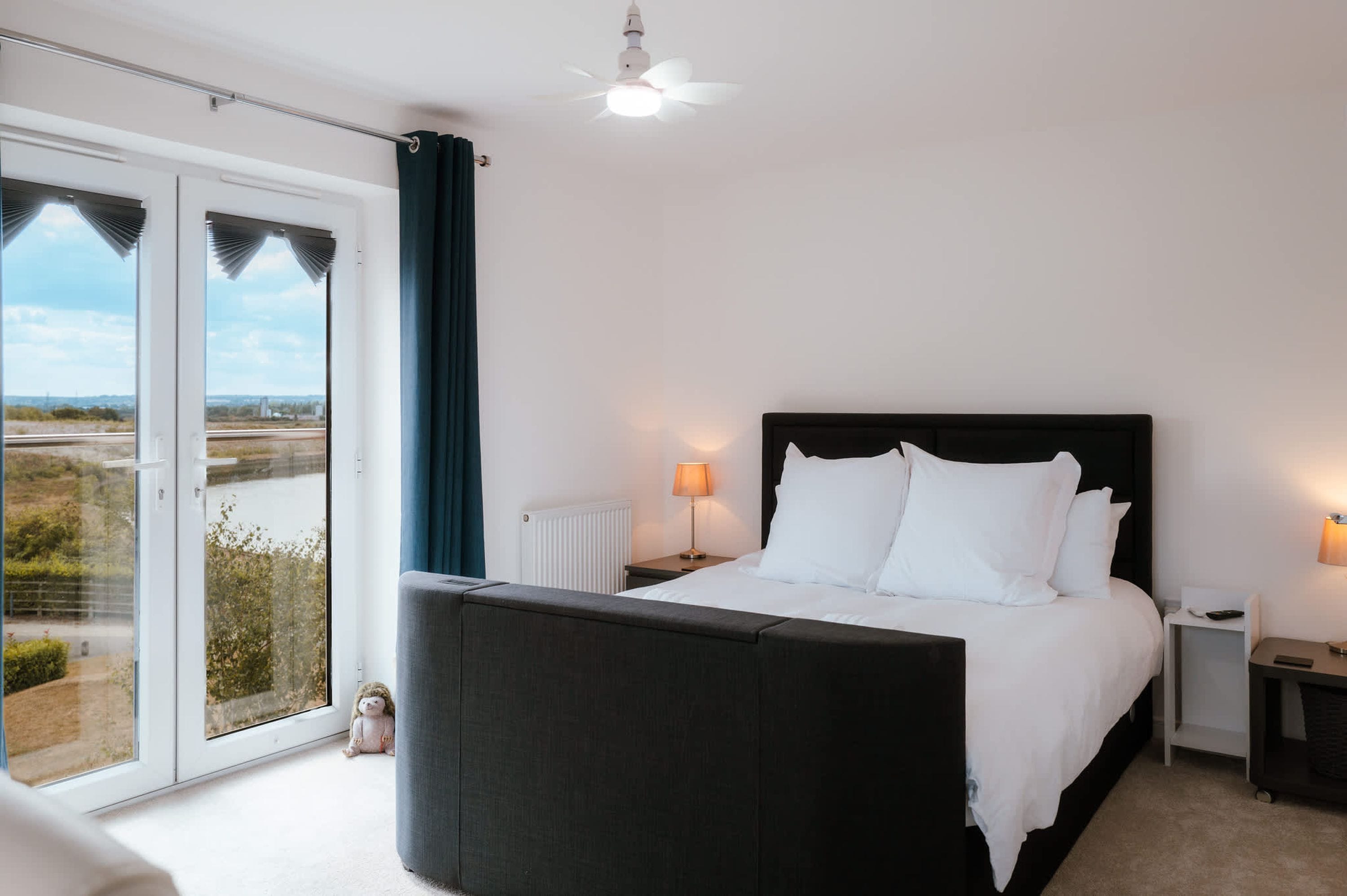 Un dormitorio con una cama grande, dos mesitas de noche, un ventanal con cortinas y vistas al exterior.