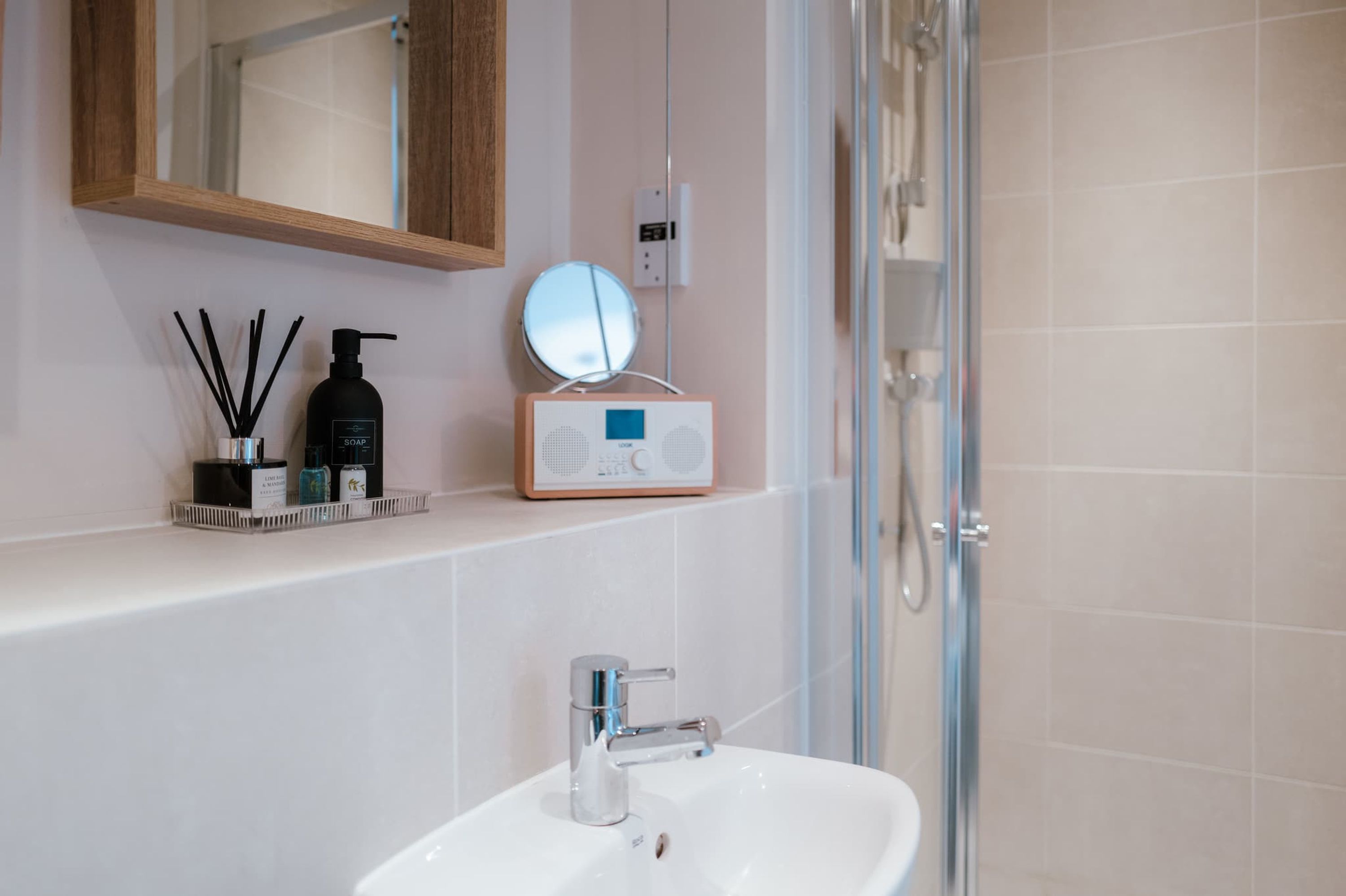 A bathroom with a white sink, a mirror, a soap dispenser, and a shower.