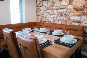 A dining area with a stone wall, brown leather booth seating, and a wooden table set for four. - Perfect Booking Spacious 3-bed Home w Garden (Rochester)