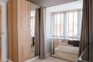 A room with a sliding door, a window with blinds, a mirror, and a small table. - Perfect Booking Spacious 3-bed Home w Garden (Rochester)