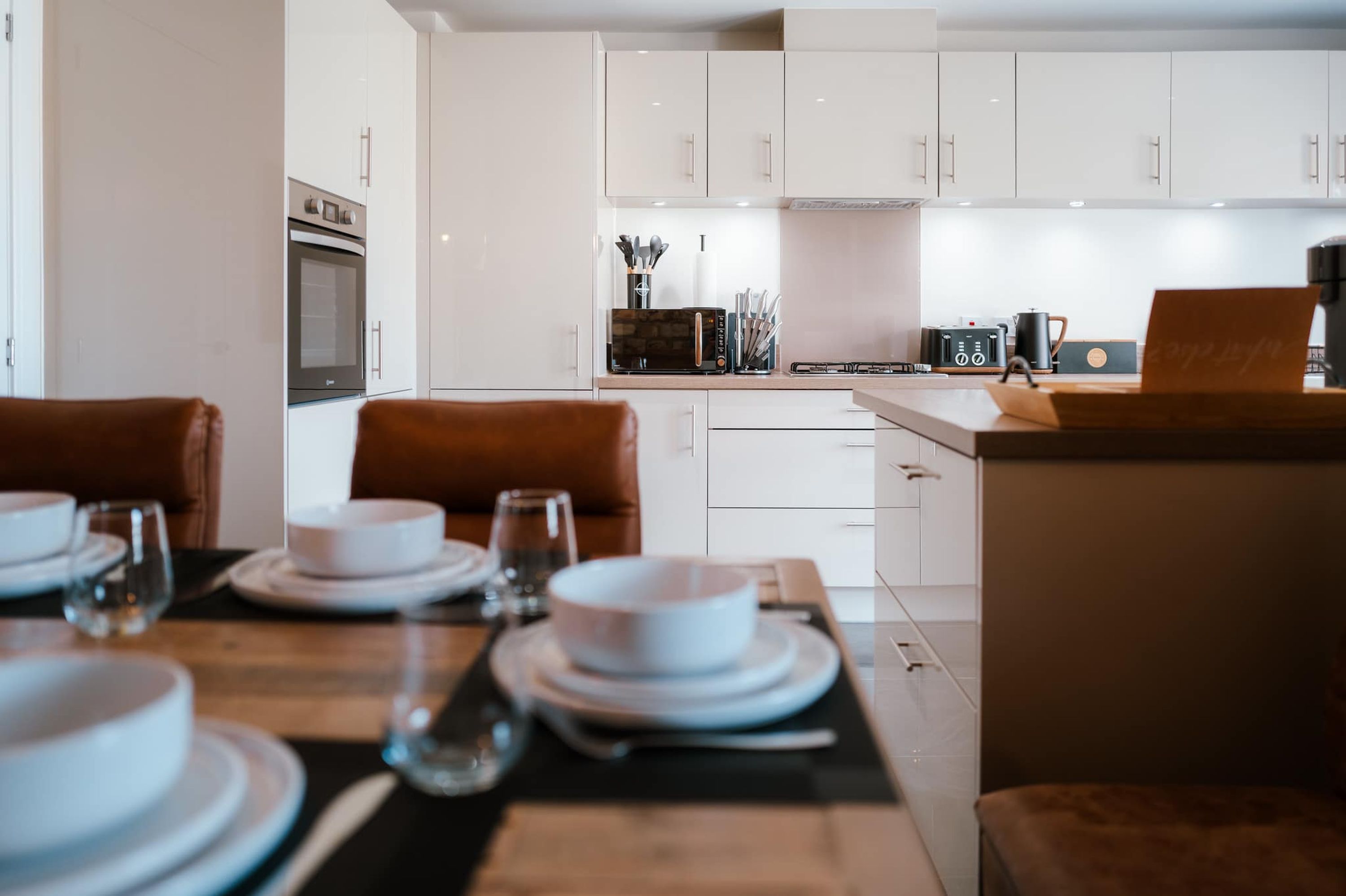 A modern kitchen with white cabinetry, a dining table set with plates and glasses, and a coffee machine.
