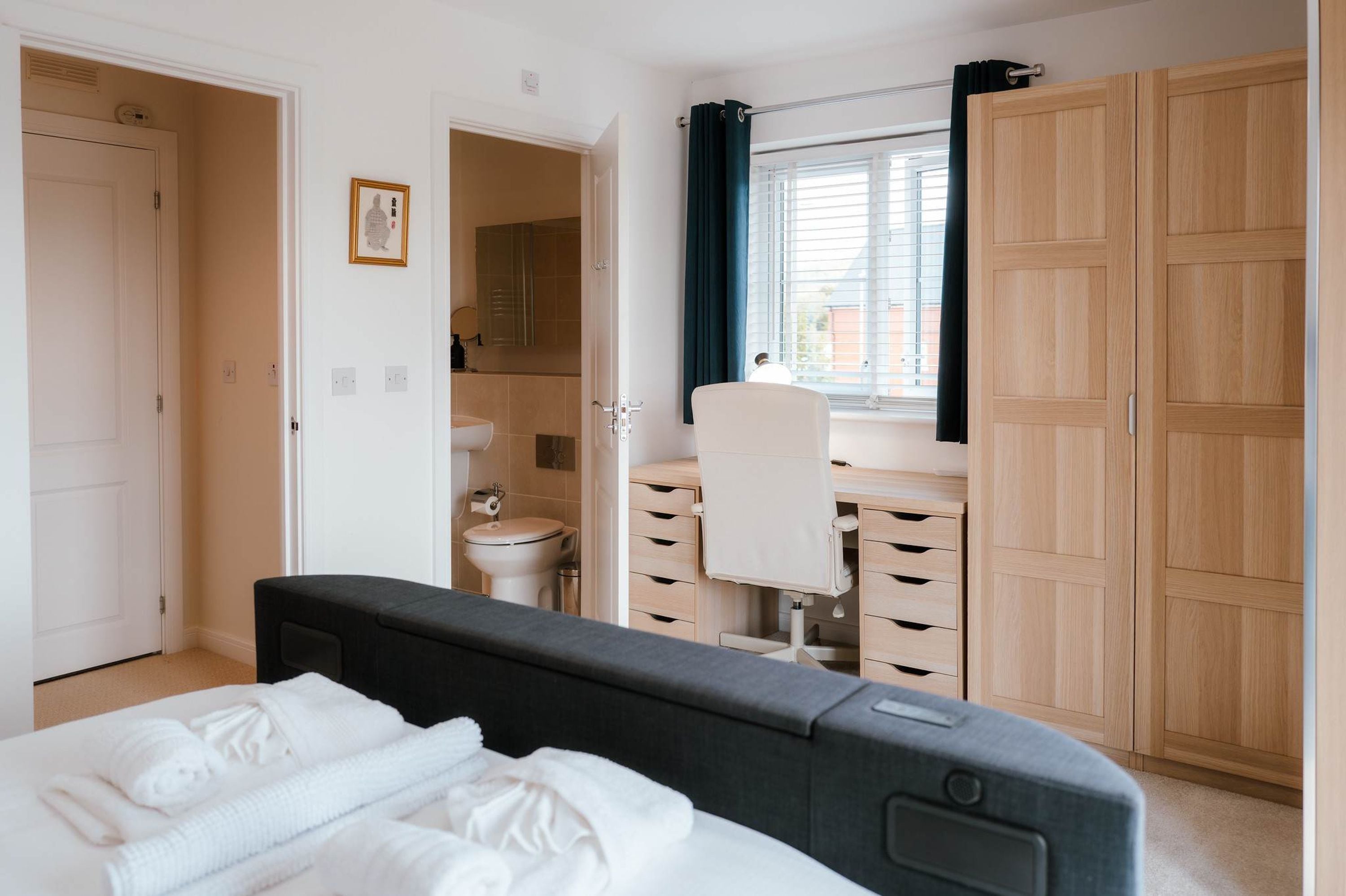 Een slaapkamer met een bed, een bureau, een stoel, een kledingkast, en een badkamer zichtbaar door een geopende deur.