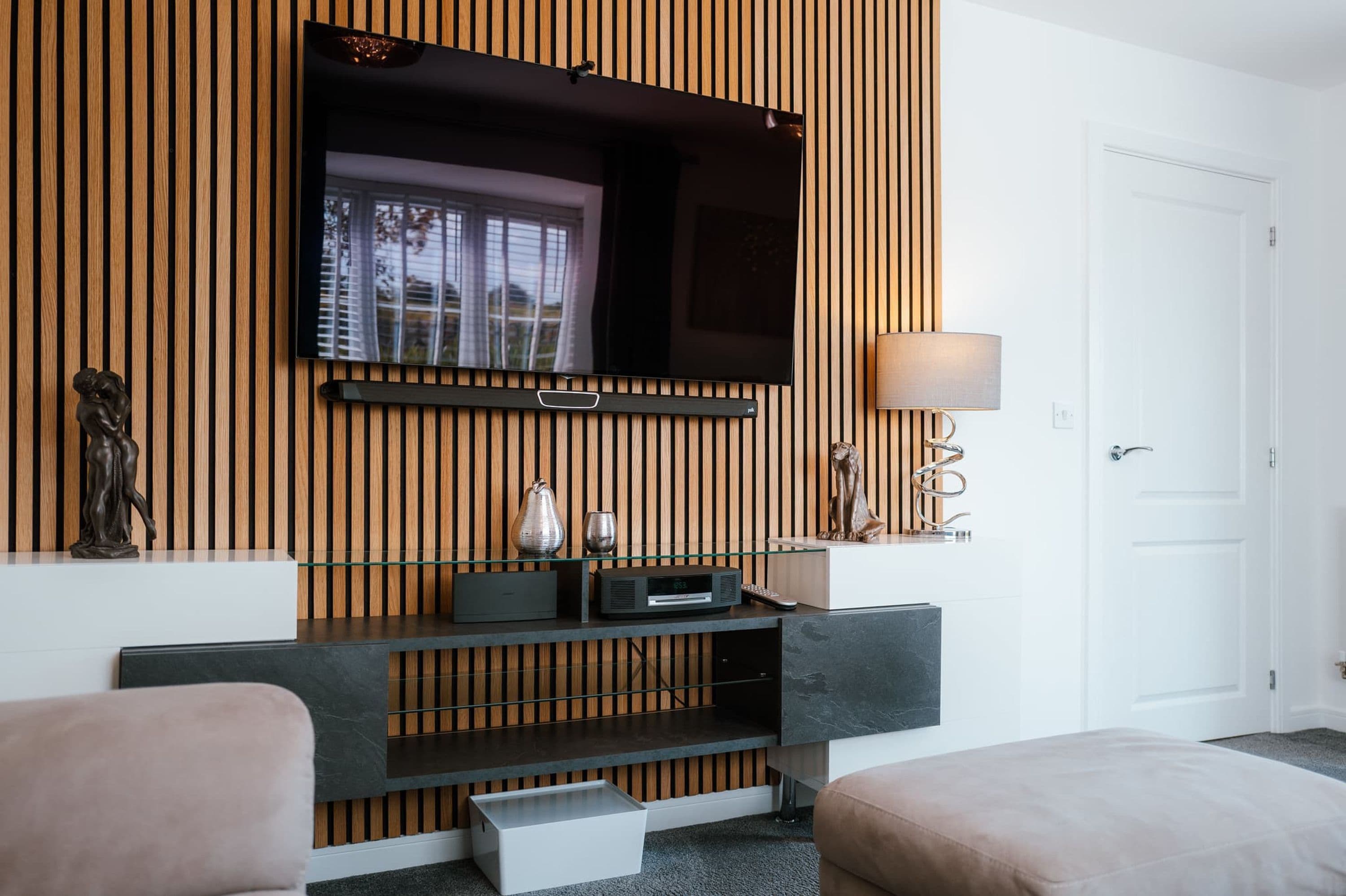 Uma sala de estar moderna com televisão de tela plana fixada em uma parede de madeira, uma mesa de centro de vidro, um sofá e um abajur.