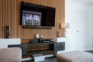 Uma sala de estar moderna com televisão de tela plana fixada em uma parede de madeira, uma mesa de centro de vidro, um sofá e um abajur.