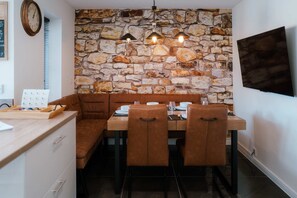 A dining area with a stone wall, wooden table, brown chairs, and pendant lighting. - Perfect Booking Spacious 3-bed Home w Garden (Rochester)