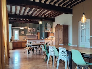 Een eethoek met een houten tafel en stoelen, een keuken achtergrond en een klok aan de muur.