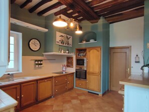 Een keuken met houten kastjes, een inbouwoven en een klok aan de muur.