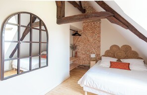 Een slaapkamer met een schuine balkenkap, een houten bed, een groot rondboogvenster en een bakstenen muur.