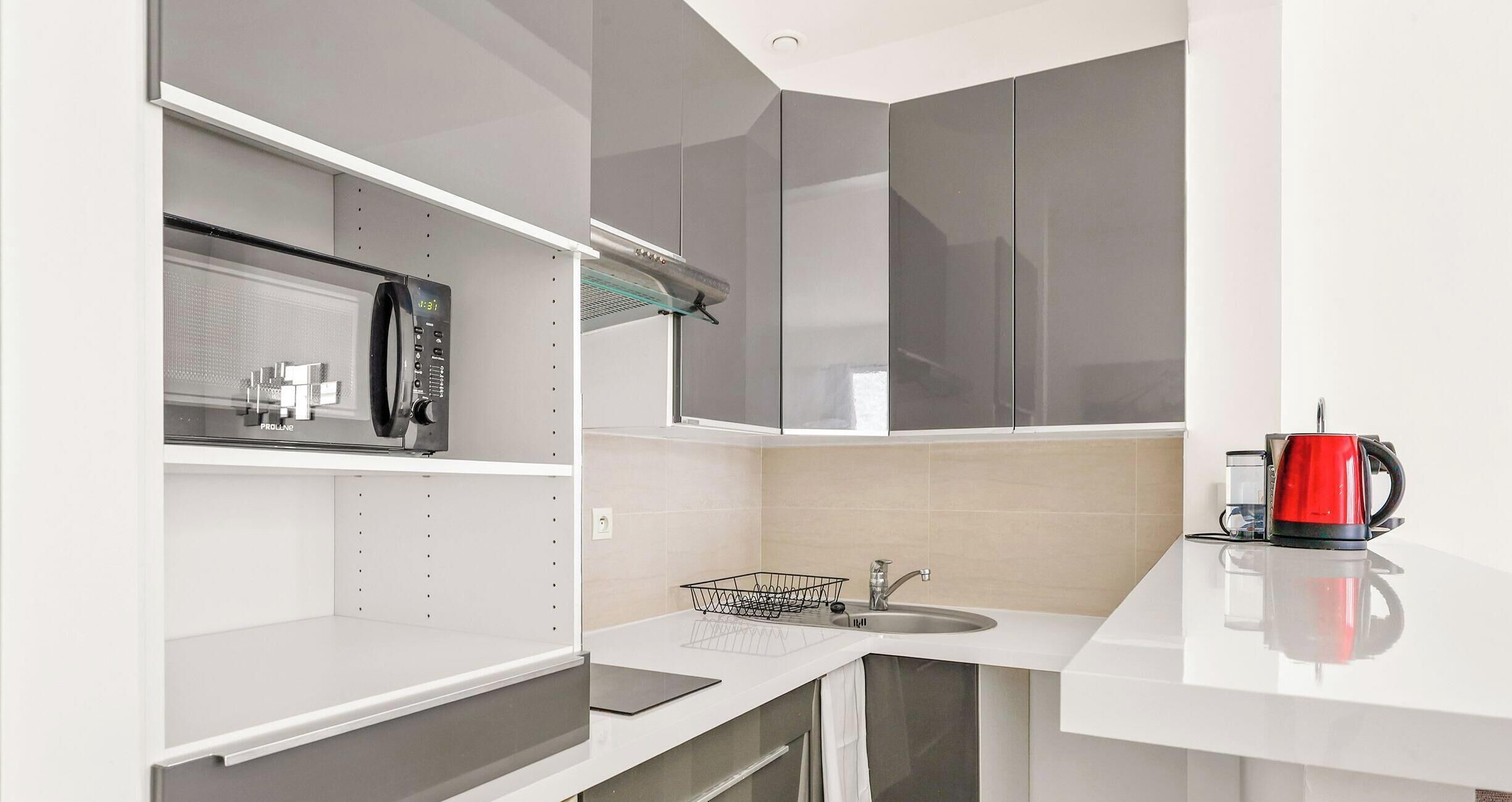 A modern kitchen with white cabinetry, a stainless steel sink, and a red kettle on the counter.