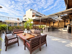 Een terras buiten met houten meubels, een grillplaats en potplanten.
