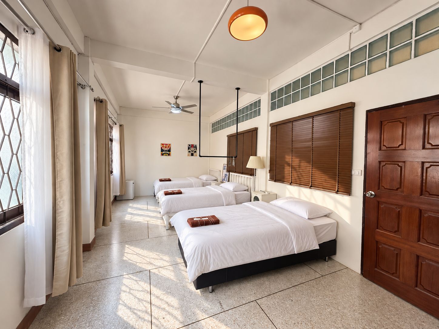 A hotel room with four single beds, a large window with curtains, a ceiling fan, and a wooden door.