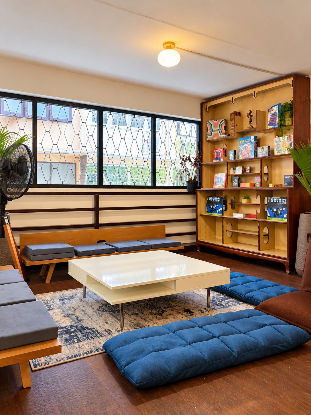 A modern living room with a white coffee table, blue cushioned seating, a wooden bench, and a bookshelf filled with books and decorative items.