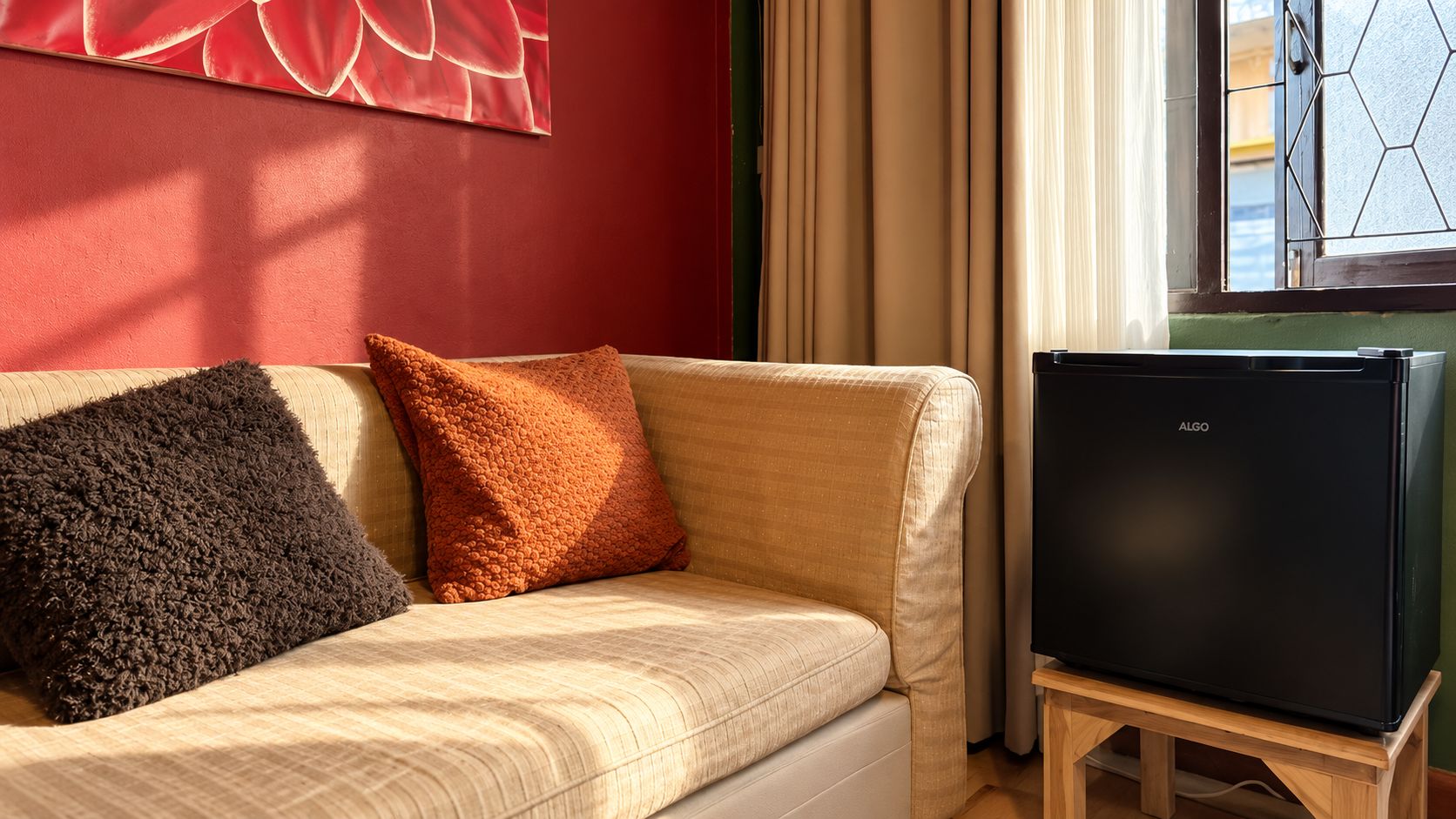A sofa with two pillows, a television on a stand, and a window with curtains.