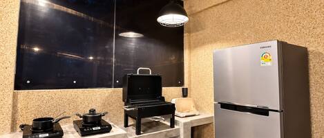 Una cocina compacta con un refrigerador de acero inoxidable, una estufa a gas portátil y un microondas.