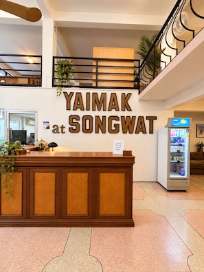 A reception desk with a sign reading 'Yaimak at Songwat' and a vending machine to the right. - Yaimak House Mid Century (Bangkok)