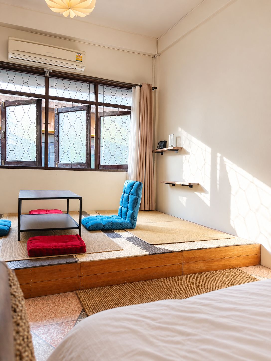 Una habitación con suelo de tatami, una silla acolchada azul, una mesita y una cama.