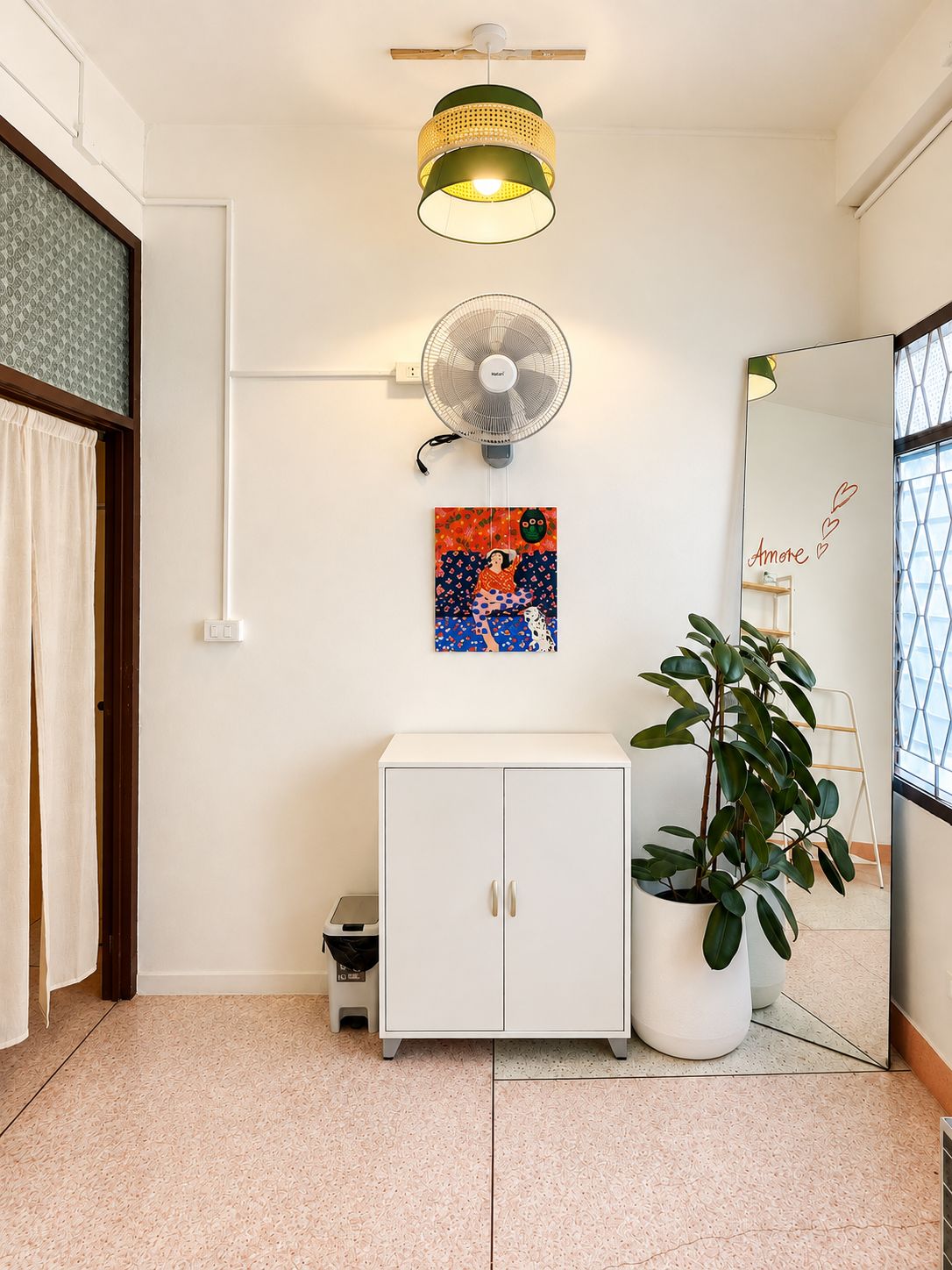A room with a white cabinet, a potted plant, a wall-mounted fan, a ceiling fan, and a painting.