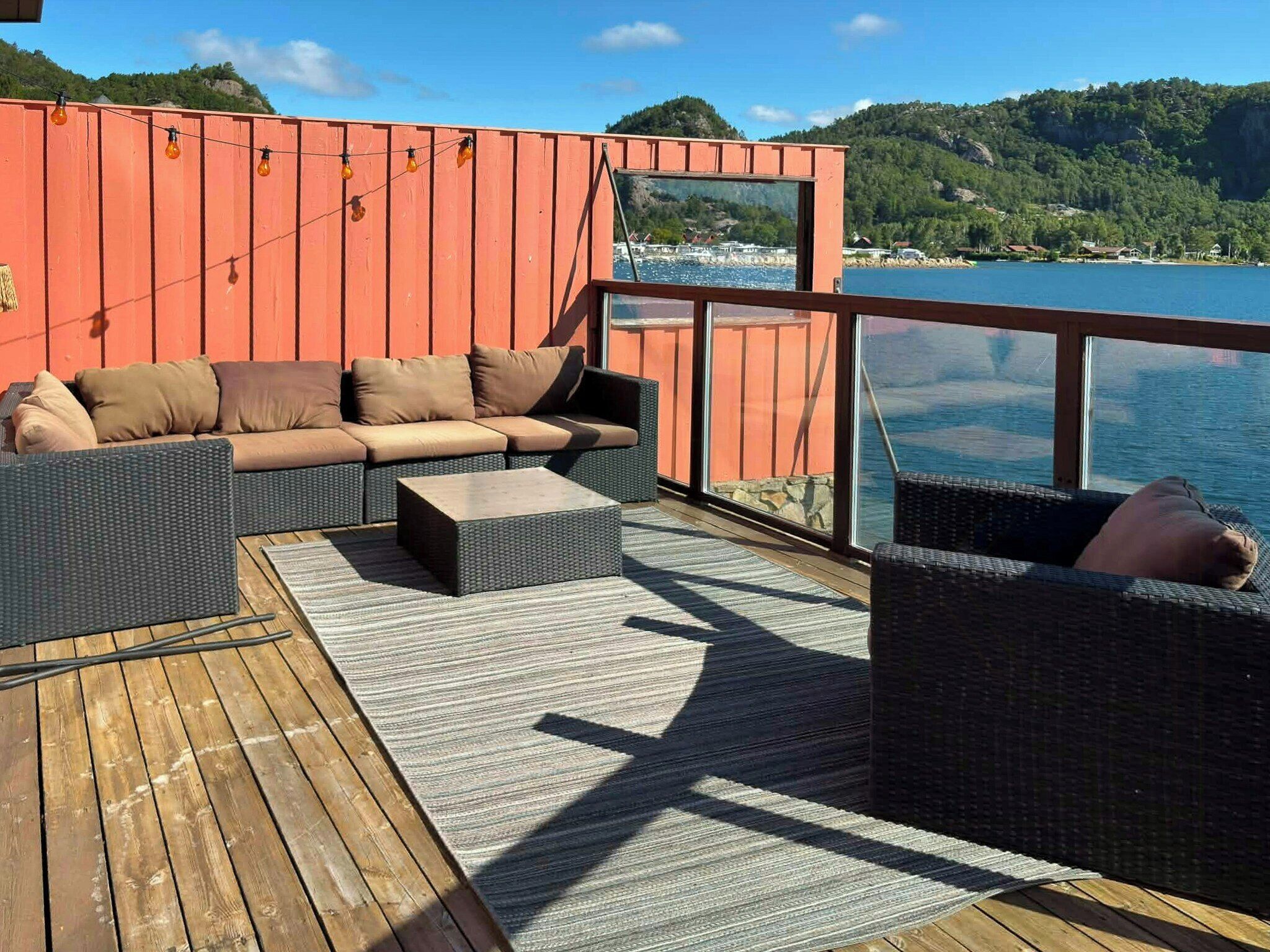 En terrass med en soffa och stolar, med utsikt över en sjö eller ett annat vattendrag och kullar.