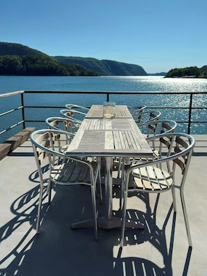 A wooden table with metal chairs on a deck overlooking a body of water with hills in the background. - Retro beach house with jetty in Åptafjorden (Farsund)