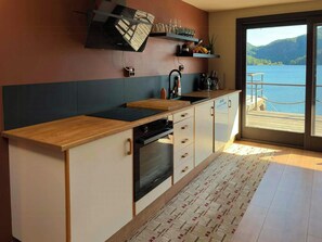 A modern kitchen with a wooden countertop, built-in oven, and a view of a lake through a sliding glass door. - Retro beach house with jetty in Åptafjorden (Farsund)