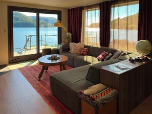 A modern living room with a large sofa, a round coffee table, and a view of a lake through large windows. - Retro beach house with jetty in Åptafjorden (Farsund)