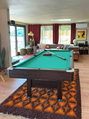 Une table de billard dans un salon, avec un canapé et une bibliothèque en arrière-plan.