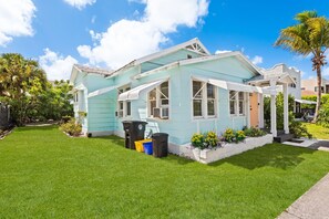 A light blue house with a white porch, surrounded by a well-maintained lawn and a variety of plants. -  2-bedroom Lake Worth Beach House; Near Downtown (Lake Worth Beach)