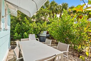 An outdoor patio with a table and chairs, surrounded by lush greenery and a barbecue grill. -  2-bedroom Lake Worth Beach House; Near Downtown (Lake Worth Beach)