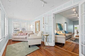A spacious living room with a large window, a sofa, a striped armchair, and a small side table. -  2-bedroom Lake Worth Beach House; Near Downtown (Lake Worth Beach)