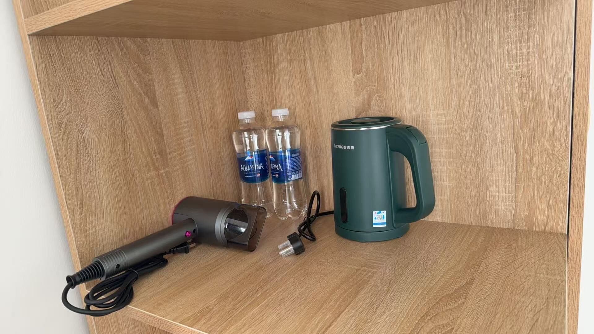 A wooden shelf with a hair dryer, two bottles of water, and a kettle.