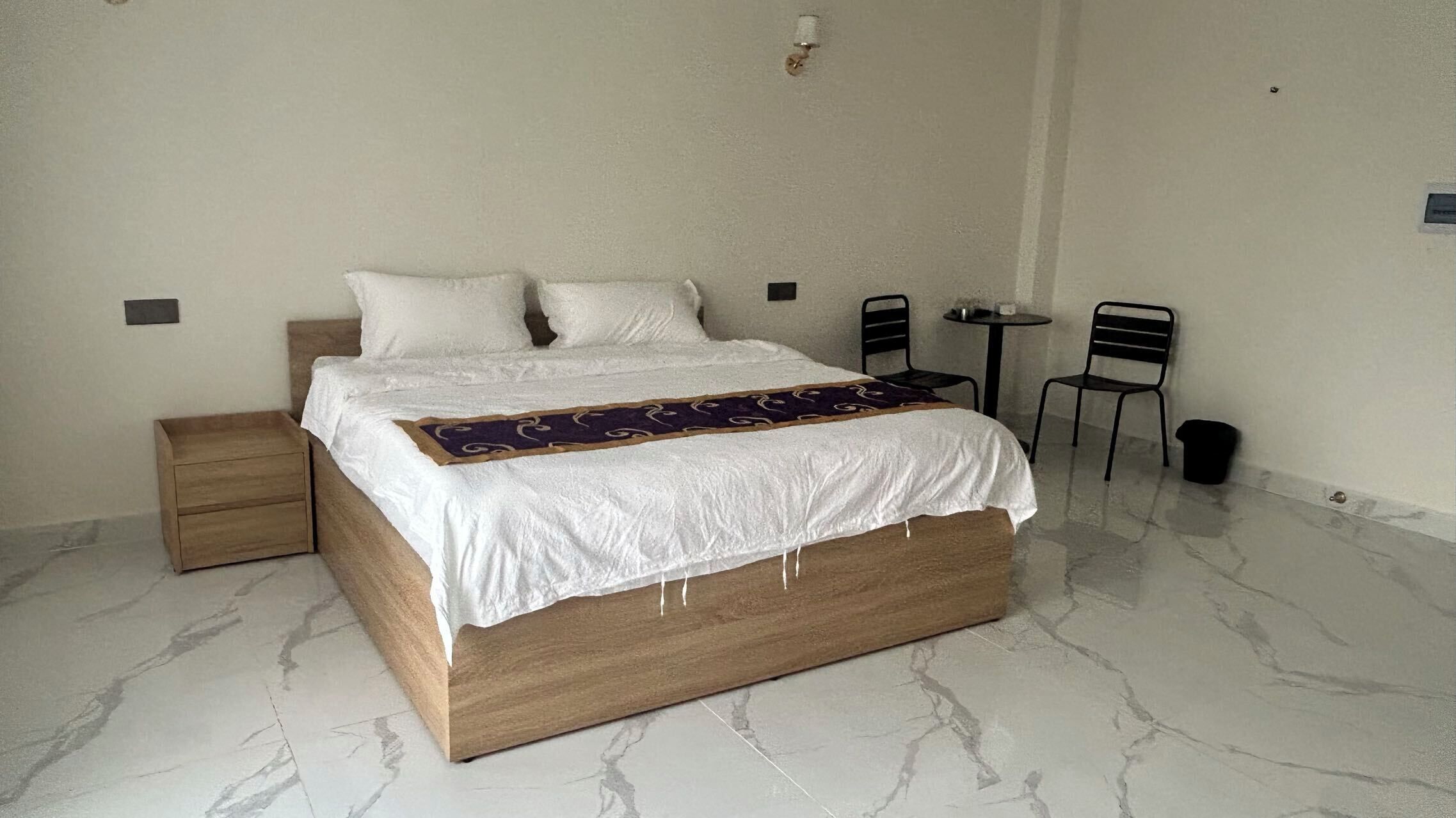 A bedroom with a wooden bed, a bedside table, a chair, and a small table.