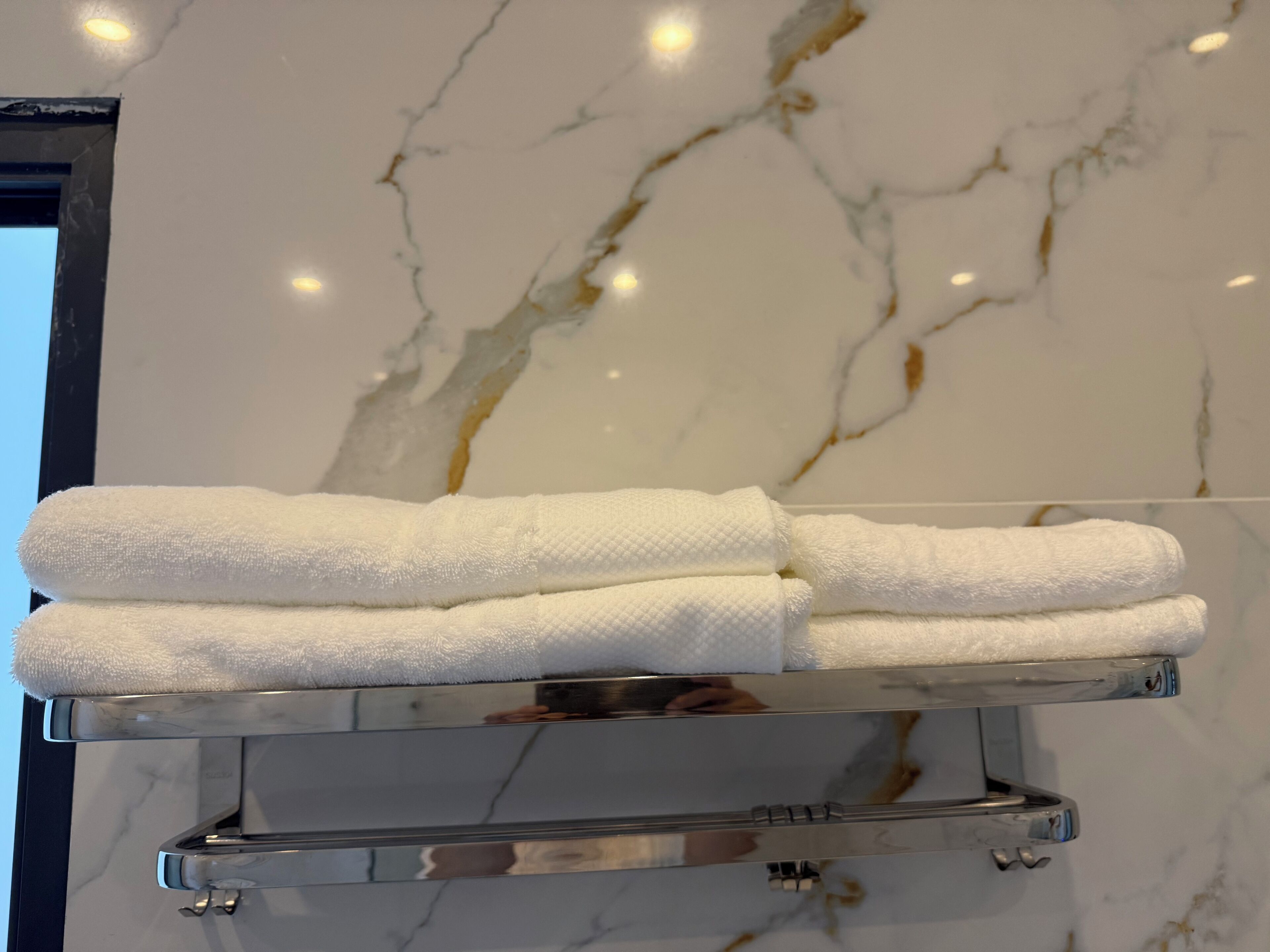A bathroom with a marble wall and a towel rack holding folded towels.