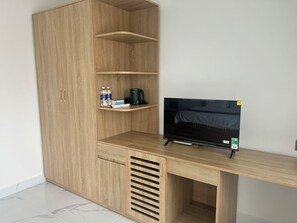 A modern room with a wooden cabinet, a TV on a stand, and a shelf with water bottles and a coffee maker.