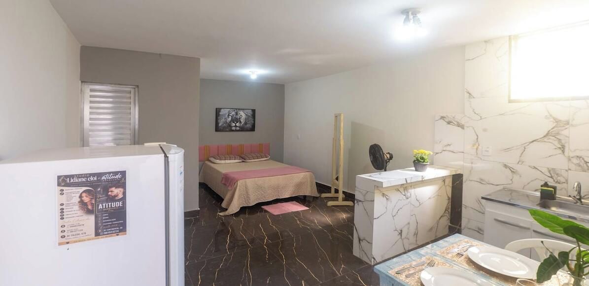A compact hotel room with a bed, a small kitchenette, a bathroom with a mirror and sink, and a refrigerator.