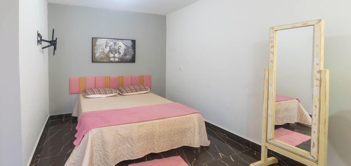 Een slaapkamer met een bed, een spiegel, een wandlamp en een lijst met een afbeelding.