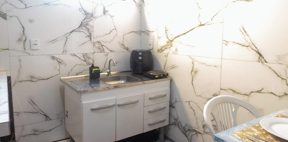 A compact kitchen with a marble backsplash, a sink, a coffee maker, and a chair.