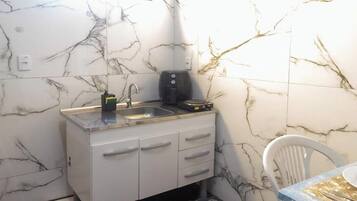 A compact kitchen with a marble backsplash, a sink, a coffee maker, and a chair.