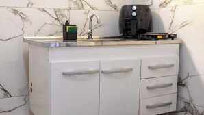 Et køkken med marmorbeklædt bagvæg, kaffemaskine og vask.