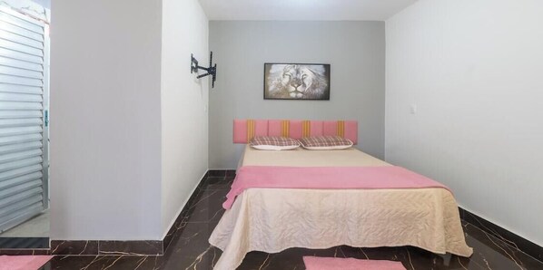 A bedroom with a bed, a headboard, a wall-mounted light, and a framed picture.