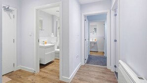 A hallway leading to a bathroom with a shower, toilet, and sink. - Modern Digbeth (Birmingham)