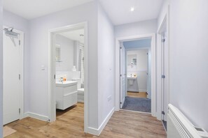 A hallway leading to a bathroom with a shower, toilet, and sink. - Modern Digbeth (Birmingham)