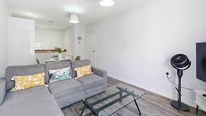 A modern living room with a grey sofa, a glass coffee table, and a standing fan. - Modern Digbeth (Birmingham)