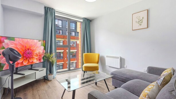 A modern living room with a sofa, a glass coffee table, a yellow armchair, a flat-screen TV, and a potted plant. - Modern Digbeth (Birmingham)