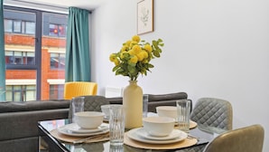 A dining area with a table set for four, a vase with yellow flowers, and a framed picture on the wall. - Modern Digbeth (Birmingham)