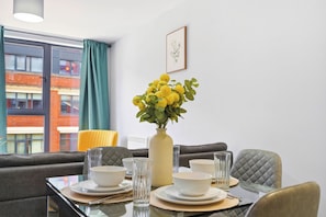 A dining area with a table set for four, a vase with yellow flowers, and a framed picture on the wall. - Modern Digbeth (Birmingham)