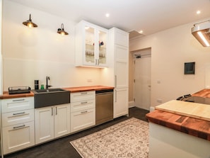 A modern kitchen with white cabinetry, a wooden countertop, and a built-in dishwasher. - Winnocklands House (Newmilns)