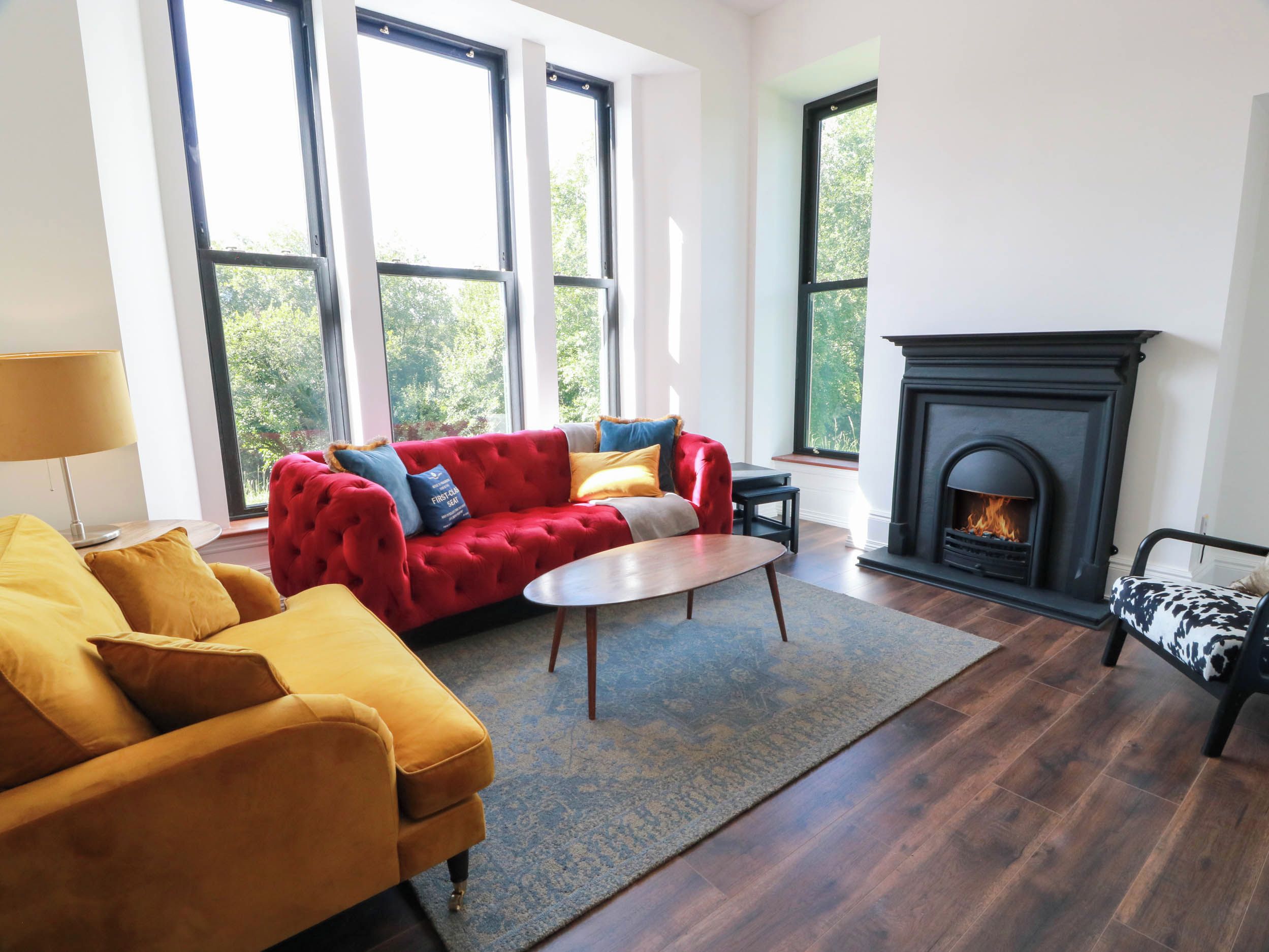 Una sala de estar con un sofá rojo, sillones amarillos, una chimenea y ventanas grandes.