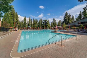 A swimming pool with a tiled deck, surrounded by trees and a building with outdoor seating. - Closest Ski-in/out Condo at Northstar Village (Truckee)